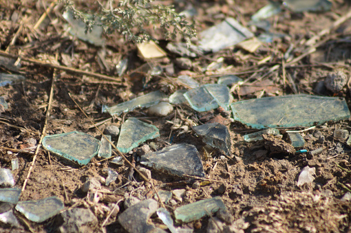 Close-up of shards of glass thrown on the ground with mud