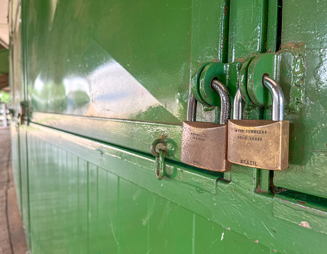 Two bronze padlocks on green metal shutters