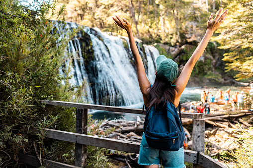 Young woman with arms outstretched in front of a waterfall in a Patagonia, Argentina