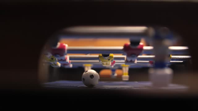 People play mini foosball and score a goal with a ball into the goal.