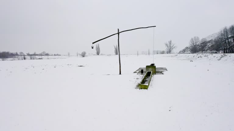 Drone captures old wooden well pump with bucket in snow covered land