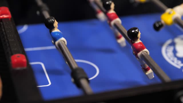 People play mini foosball and score a goal with a ball into the goal.