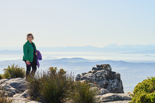 Portrait of smiling mature woman standing at a viewpoint high up on a hill with a scenic view during a summer hike