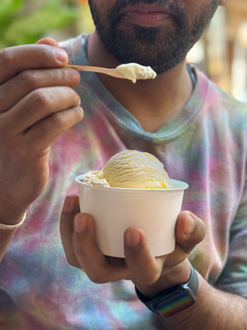 Stock photo showing a close-up view of street food dessert of scoops of vanilla ice cream served in a white, single-use, disposable, cardboard tub with wooden spoon.
