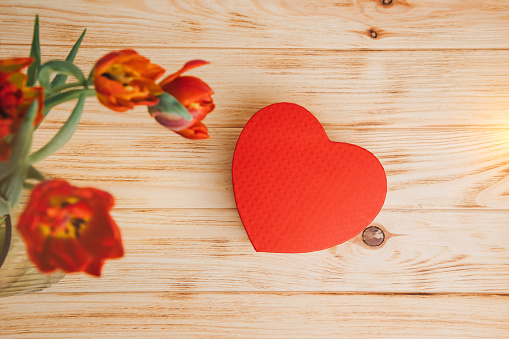 Red bouquet of tulips in a vase with red gift box in the shape of heart. Background with a bouquet of flowers. Valentine's day gifts. Top view