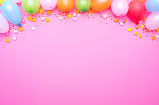 Party balloons and confetti border on pink background. Copy space