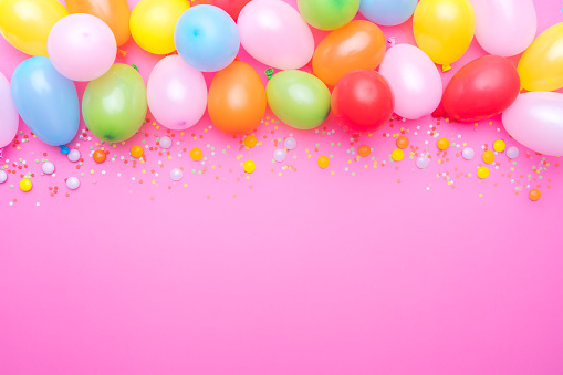 Party balloons and confetti border on pink background. Copy space