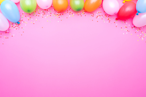 Party balloons and confetti border on pink background. Copy space