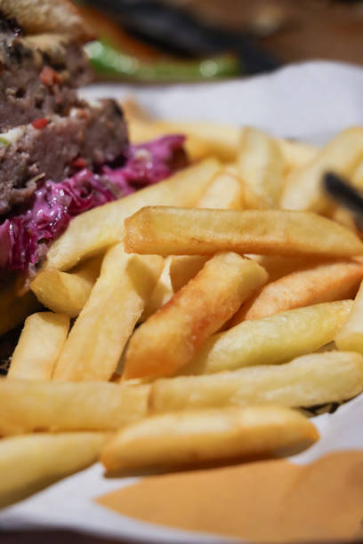 Stock photo showing close-up view of a meal of half a cheeseburger in a sesame seed bread bun served with a beef patty on bed of red cabbage coleslaw, a slice of melting processed cheese and crunchy French fry chips.