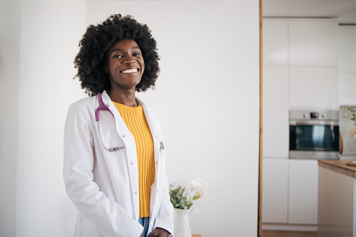 Portrait of an African young doctor standing and smiling,in the background is the kitchen