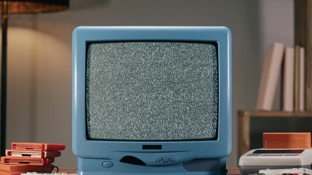 Old television with grey interference screen on home background. Close-up of vintage tv and cartridges for retro playstation. Antique video game, nostalgia.