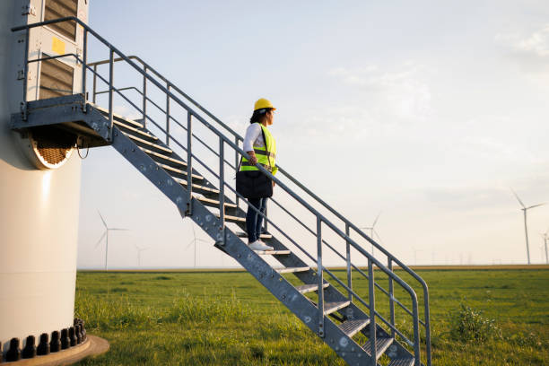 istock Female Engineer wearing uniform ,helmet hold document inspection work in wind turbine farms rotation to generate electricity energy 1990564652