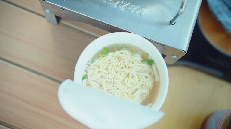 Overhead view of instant noodles being prepared with steaming hot water poured from an electric kettle, Hot water pouring into a cup of instant noodles, a quick meal preparation