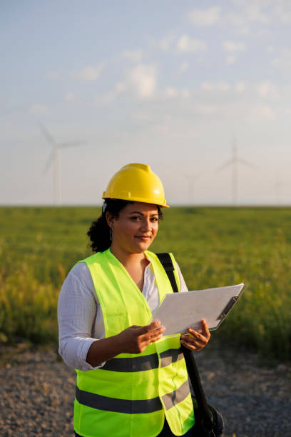 istock Female Engineer wearing uniform ,helmet hold document inspection work in wind turbine farms rotation to generate electricity energy 1990572768