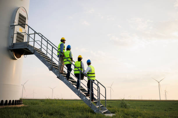 Engineers wearing uniform ,helmet hold document inspection work in wind turbine farms rotation to generate electricity energy.