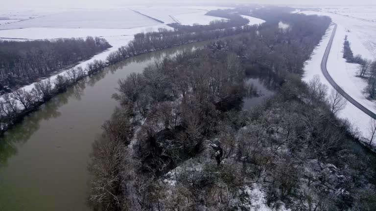 Aerial view wooded land on a shore of two rivers in winter while snow falls