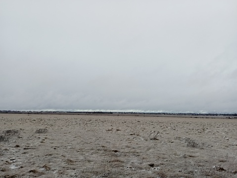 Snow storm on the horizon. Large drifts of snow far beyond the horizon. The gloomy sky over the steppe covered with dry grass sprinkled with wet snow.