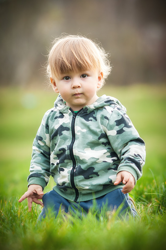 Cute baby boy having fun sitting on grass in sunshine day. Spring time, happy baby