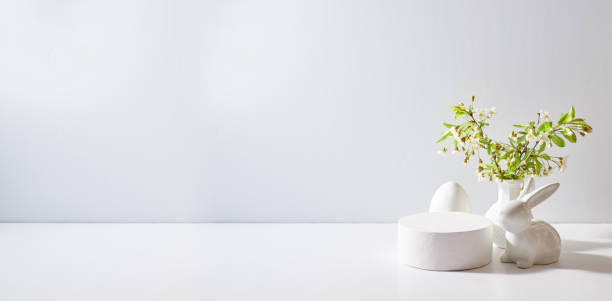 istock Empty round white podium for product presentation. Spring flowers in a vase and easter eggs on a light background 1990643885
