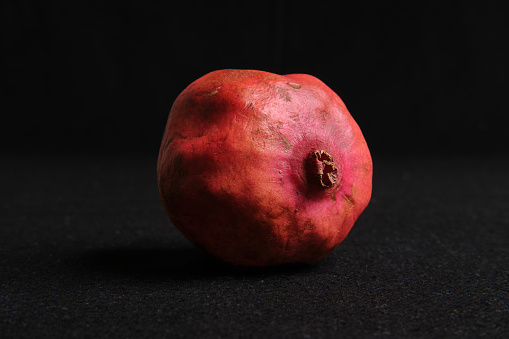 A solitary pomegranate rests against a dark backdrop, its rich, red skin glowing with an enigmatic allure.