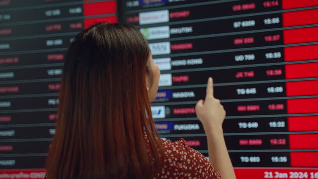 The young Asian woman is checking the flight information on the boarding board at the airport.
