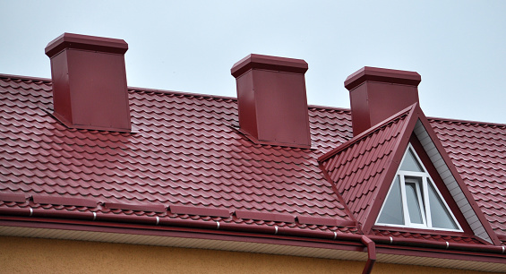 A chimney on the roof of a house covered with metal tiles or a metal profile