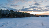 The setting sun on the horizon over a pine forest and lake. Evening winter landscape with contrasting cloudy sky