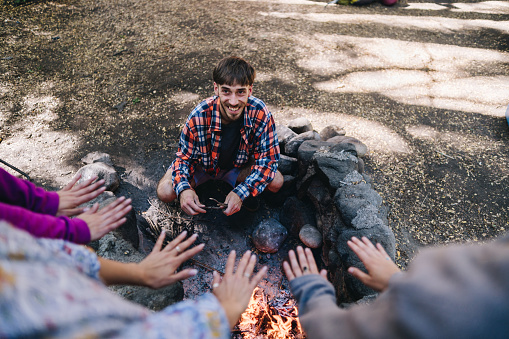 Friends warming hands over campfire at forest camp