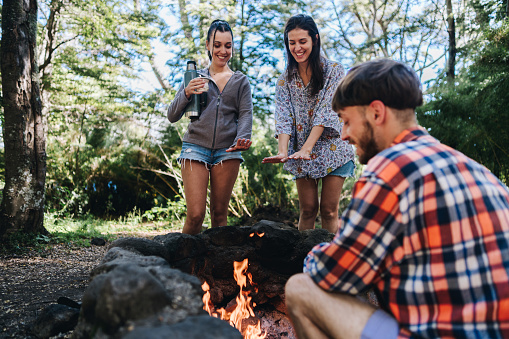 Friends warming hands over campfire at forest camp