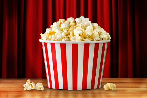 Popcorn in red and white striped paper bucket on a red curtain background. Popcorn on wooden bar counter in Movie theater.