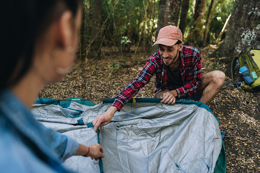 Young man setting up tent for camping with friend in the forest