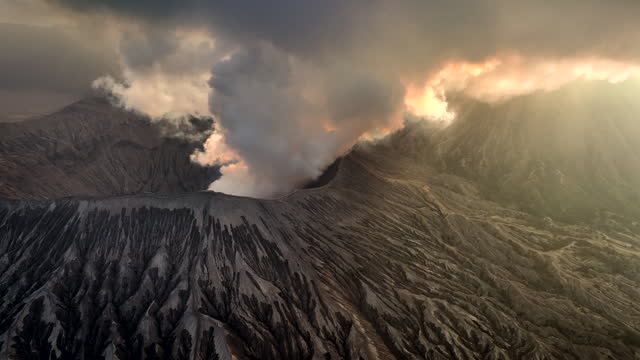 Aerial Drone Sunset Scene of Eruption Cover Volcano Mts. Bromo surrounded by Cloud, Fog and Smoke with mount Semeru, Batok and Widodaren, Tengger Caldera, Indonesia