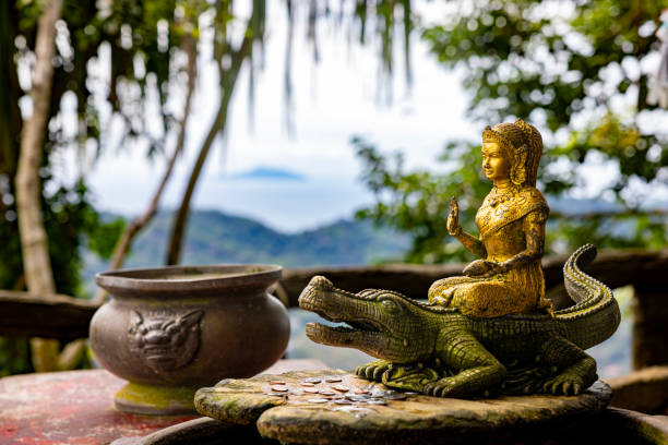 Stone buddha statue stands serenely in lush green garden, radiating peace and tranquility under the soft light of a cloudy day.