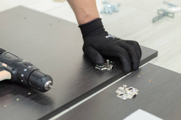 istock A worker installs hinges on a pair of wooden cabinet doors. carpinteria concept. 1990868070