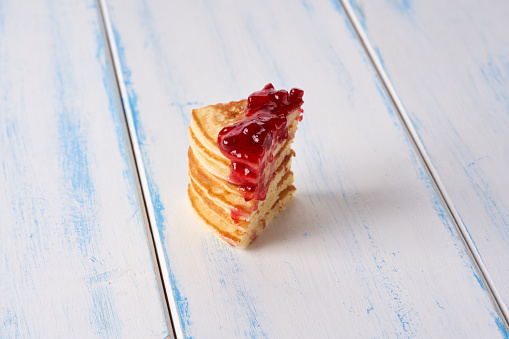 Pancakes with red berry jam on the wooden table.