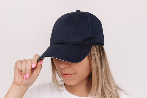 Young caucasian blonde woman holding the visor of the cap showing empty copy space for design or text on a white background