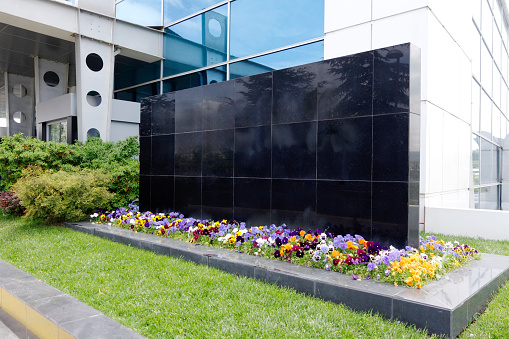 Granite-covered sign wall outside a hospital building. Decorated with grass and flowers. No people.
