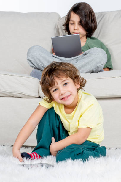 little boy is playing with tablet on the carpet on the floor. - looking at camera full length outdoors image technique foto e immagini stock