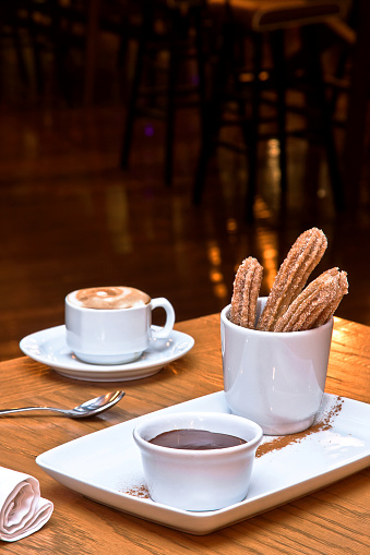 churros with sugar and chocolate for soaking, cappuccino coffee on wooden table in restaurant