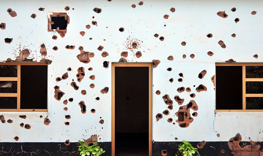 Kigali, Rwanda: bullet ridden façade - war torn, ravaged white wall filled with bullet impact marks - pockmarked brick masonry - an old military installation, preserved as it was after the 1994 Rwandan genocide, outside which 10 Belgian United Nations peacekeepers were executed by the presidential guard. Belgian peacekeepers memorial.