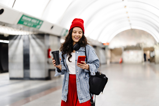 Beautiful woman walks down the subway station and uses smart phon. She is happy and smiled.