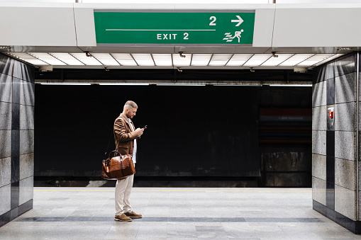 Man walks down the subway station and uses smart phone.