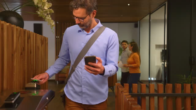 Latin American businessman leaving the office and scanning his card at the door on a turnstile while texting on smartphone