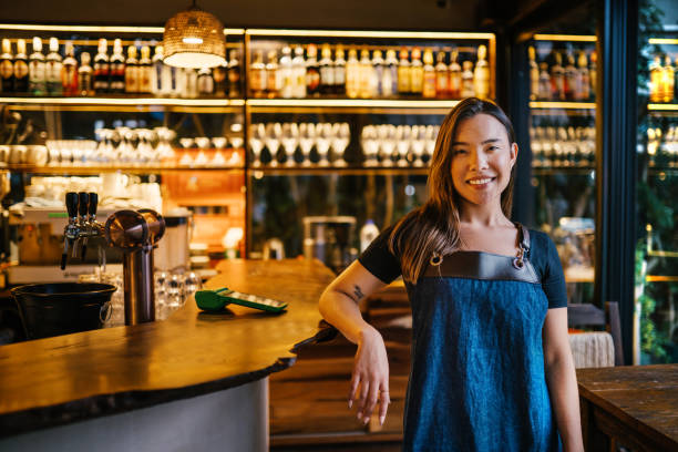 istock Smiling young bartender leaning on the checkout counter in a trendy bar 1991021400
