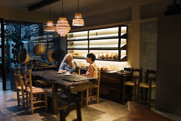Two smiling mature female friends talking together over coffee at a table on a trendy cafe and bakery