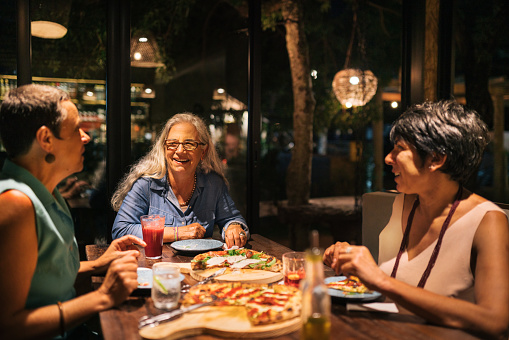 Smiling group of mature female friends talking together while eating pizza in an Italian restaurant in the evening