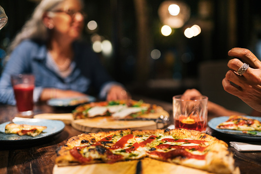 Close-up of a pizza sitting on a table during a dinner with a group of mature female friends in a restaurant