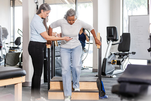 The female physical therapist stands close by to support her female patient as she practices using the stairs.