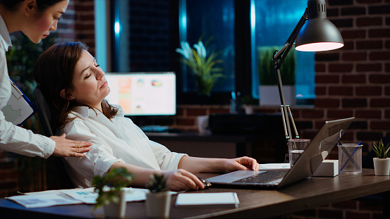 Tired employee sleeping on workspace desk, awaken by manager, excusing herself. Drowsy businesswoman woken up by team leader after napping in office working overnight, feeling ashamed, camera B