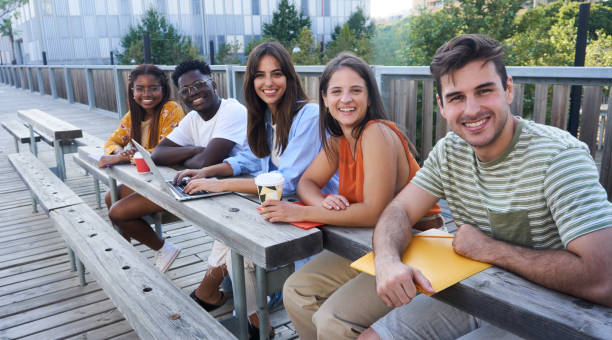 Group of multiethnic student sitting together outside university to do schoolwork looking at camera